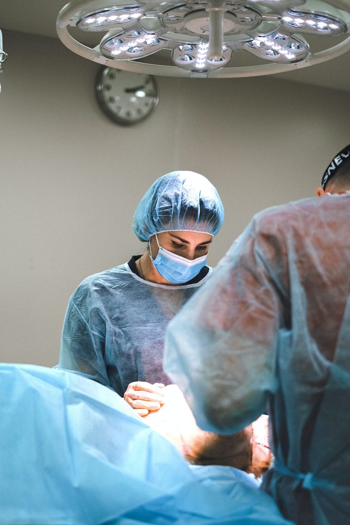 Konzentrierte Chirurgin in blauer Haube und Maske bei einer Operation